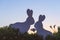 Creative photo of two silhouette paper rabbits in the chamomile flowers and green grass on the sunset sky background