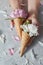 Creative post card of wafer cones with gentle peony flowers in a girls hands with petals on a gray concrete background.