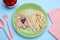 Creative serving for kids. Plate with cute dog made of tasty pasta, sausage and cucumber on light blue table, flat lay