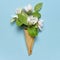 Creative spring minimal concept. Waffle cone with bouquet of spring blooming branches of white flowers and green leaves on blue