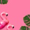 Creative summer beach concept. Inflatable pink mini flamingo and tropical leaf monstera on pink background, pool float party. Flat