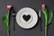 Creative table setting with hearts on a white plate  black fork and knife  tulips on a dark background.