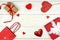 Creative Valentine Day romantic composition with red hearts, satin ribbon, lollipop, gift box and paper bag on white background.