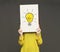 Creativity and innovations. Young woman holding poster with drawing of light bulb in front of her face, grey background