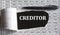CREDITOR is the word behind torn office paper with numbers and a black pen