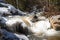 A creek runs past ice and snow covered boulders