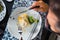 Crepe covered in white sauce lying on plate with broccoli pieces, man eating as seen from above, classy table setting