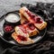 Crepes with cottage cheese, fruit jam, cherries, sour cream and icing sugar on black plate over dark background. Top view