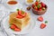Crepes, traditional Russian thin pancakes on a white plate with fresh strawberries and honey on a light background.