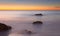 Crescent moon at sunrise with beautiful red sky, calm sea with rocks in foreground, port nou, cala bona, mallorca, spain