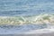Cresting breaking wave on shoreline edge with washback foam on sandy shoreline