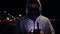 a criminal bandit hacker in a balaclava at night on the street uses a phone for illegal activities