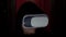 Criminal programmer in hood using VR glasses in dark room close up