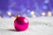 Crimson Christmas ball on white knitted fabric on purple background with warm bokeh.