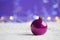 Crimson Christmas ball on white knitted fabric on purple background with warm bokeh.
