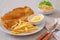 Crispy fish and chips on white plate and vegetable salad in bowl