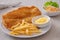 Crispy fish and chips on white plate and vegetable salad in bowl