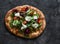 Crispy focaccia with mozzarella, cherry tomatoes, arugula, radicchio salad on a dark background, top view