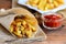 Crispy potato fries. Oven baked sweet potato fries in paper and white plate, tomato sauce. Wooden table. Rustic style. Closeup