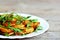 Crispy roasted potatoes with arugula on a white plate. Wooden background. Easy vegetable side dish made with potatoes and arugula