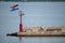 Croatian flag flying in wind on lighthouse in harbor, daytime, stone pier, man, facing away looking over stone wall