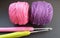 Crochet needles and yarn in pink and purple over black backdrop.