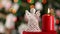 Crocheted xmas angel and burning candle on blurry christmas tree background