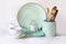 Crockery, tableware, utensils and other different white and turquoise stuff on white table-top.