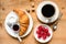 Croissant, black coffee, raspberries and jam on wooden table