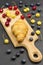 Croissant on cutting board. Blueberries, red and yellow cherries on table