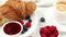 Croissant with jam and berries. Delicious and traditional breakfast in a plate on a white table