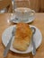 Croissant and overflow hot coffee latte in white cup on brown wooden table in coffee shop