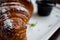 Croissant in powdered sugar on a white plate. apricot jam in a black little plate next to a croissant