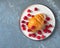 Croissant with raspberry filling and icing and fresh raspberries on a light round plate