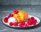 Croissant with raspberry icing and raspberries on a round plate on a gray background