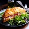 Croissant sandwich. Fresh croissant filled with ham, melted cheese and arugula salad on dark plate on wooden table at restaurant.