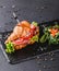 Croissant sandwich with prosciutto, tomatoes, cheese parmesan and greens on black shale board over black stone background