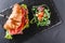 Croissant sandwich with prosciutto, tomatoes, cheese parmesan and greens on black shale board over black stone background. Healthy