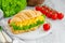 Croissant with scrambled eggs, lettuce and cherry tomatoes on a white plate with ingredients to cook on a wooden background.