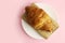 Croissant in a white plate on a pink, colored background