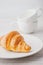 Croissant on the white plate with two blurred cups vertical