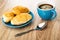 Croissants in blue saucer, cup with coffee, spoon on wooden table