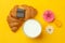 Croissants, milk, flowers and chocolate on yellow background