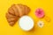 Croissants, milk, flowers on yellow background