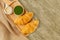 Croissants on wooden bread cutting board and sweetened condensed milk, green tea mug, with sackcloth over cement background.