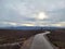 Crooked empty country road passes through autumn fields against the background of mountains