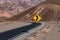 A crooked road sign along a highway curving through a barren and rugged desert landscape