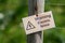 A crooked sign warning people that an electric fence is present. The sign is attached to a wire fence with a green background