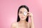 Crop attractive young female cleansing face with a cotton pad on a pink background in studio