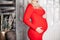 Crop of blond pregant woman in fashionable red dress embracing stomach.